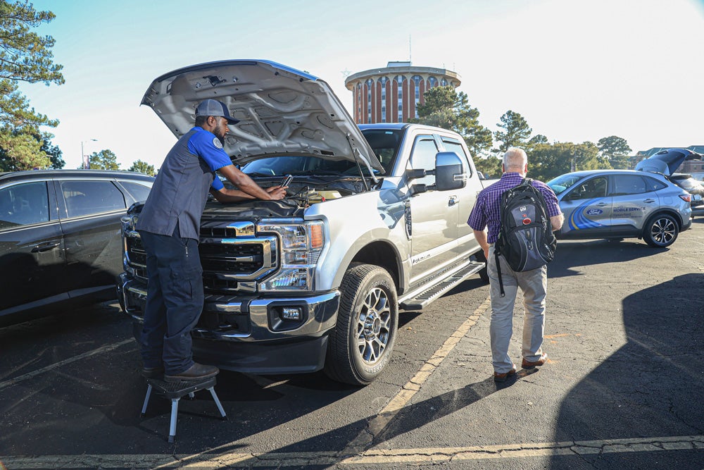 Mobile service tech checks truck in SFA parking lot as truck's owner walks to class.