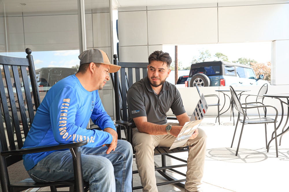 Kevin Serafin sits with customer on outdoor rocking chairs.